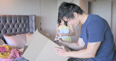 Diverse couple spotting empty box, sorting and folding clothes, labeling moving Stock Footage 342596930