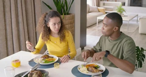 Diverse couple starting dinner at table, cutting and tasting roasted meat with Stock Footage 337286386