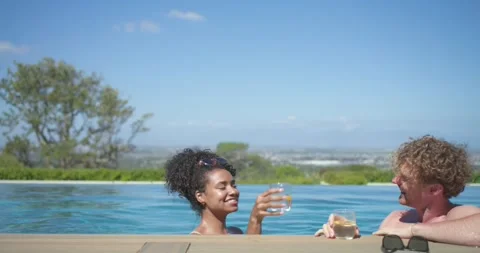 Diverse couple surfacing at infinity pool, adjusting sunglasses, lifting lemon Stock Footage 341320612
