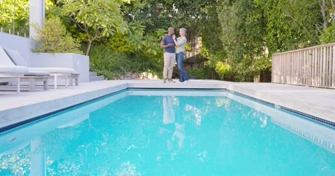 Diverse couple talking and gesturing, stepping closer at poolside by blue pool Stock Footage 336686710
