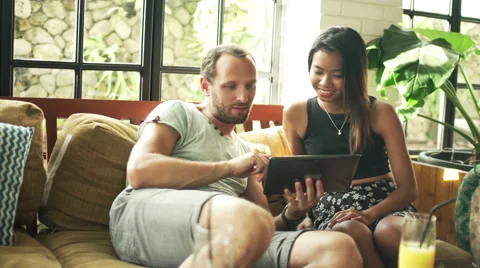 Diverse couple talking over tablet computer while sitting in cafe Video stock 53052940