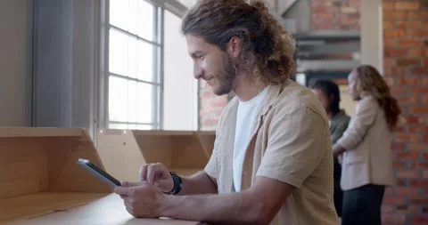 Diverse coworkers conversing in loft while man tapping tablet at counter, Stock Footage 339960729