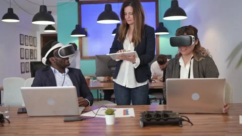 Diverse coworkers exploring virtual reality while browsing laptops Stock Footage 269353585