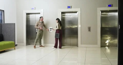 Diverse coworkers walking into elevator, pressing call panel, reviewing Stock Footage 336058374