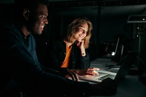 Diverse creative business people working with laptop overtime at night in low Stock Photos