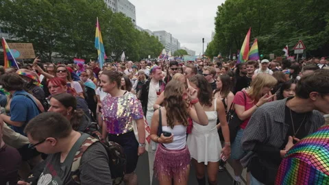 A diverse crowd of pride attendees walks through the city street holding rainbow Stock Footage 346239272