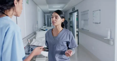 Diverse doctor and nurse using tablets and talking in corridor at hospital, in Stock Footage 339556472