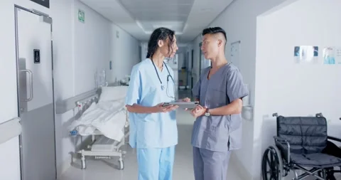 Diverse doctor and nurse using tablet and talking in corridor at hospital, in Stock Footage 344330426