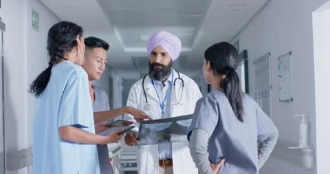 Diverse doctors and nurses using tablet and talking in corridor at hospital, in Stock Footage 341392896