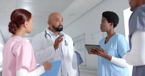 Diverse doctors discussing work and using tablet in corridor at hospital, slow Stock Footage 244982393
