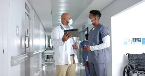 Diverse doctors discussing work and using tablet in corridor at hospital, slow Stock Footage 344534406