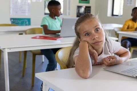 Diverse elementary students sitting at classroom desks using laptops with red Stock Photos