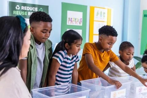 Diverse elementary students sorting recyclables into clear bins on classroom 스톡 사진