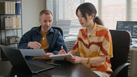 Diverse Employees Analyzing Business Papers at Table with Laptop in Office Stock Footage 335750330