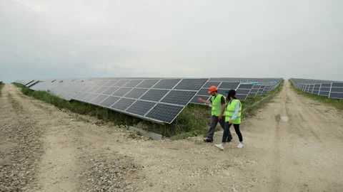 Diverse engineers in special uniform walking through solar farm. The rows of Stock Footage 156813065