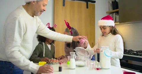 Diverse family cracking eggs and sifting flour on kitchen island for holiday Stock-Footage 337624070