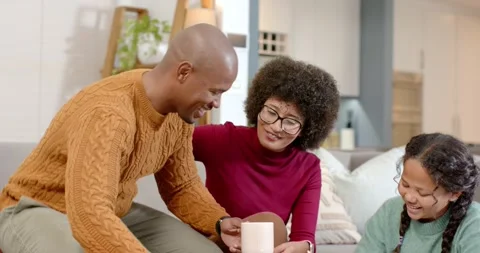 Diverse family working on homework using tablet while father bringing mugs 库存影片 344382986