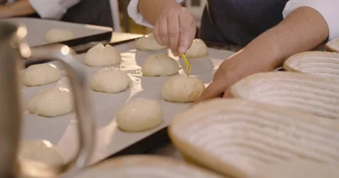 Diverse female bakers aproned tapping, scoring dough on tray at bakery with Stock Footage 344105902