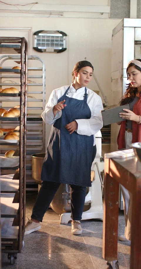Diverse female bakery team chef pointing at rack while manager tapping tablet Stock Footage 345130632