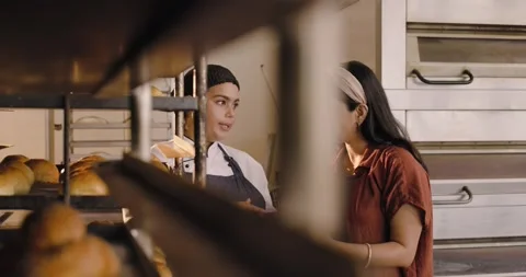 Diverse female chef and manager inspecting fresh loaves on racks in bakery, Stock Footage 342393356