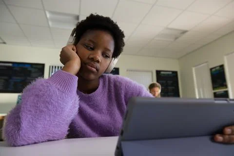 Diverse female classmates sitting in computer lab using tablet with headphones Stock Photos