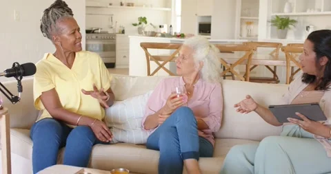 Diverse female cohosts on sofa checking tablet notes after left host leaning and Stock Footage 341852364