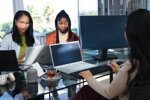 Diverse female colleagues collaborating on code at glass table with three Stock Photos