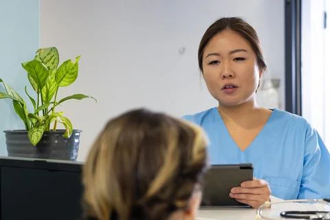 Diverse female doctor with tablet and receptionist talking at hospital rece.. Stock Photos