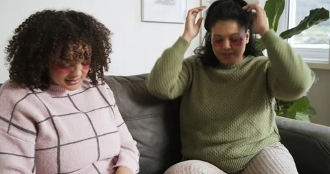 Diverse female friends applying hydrogel patches on sofa tapping phone and Stock Footage 337623973