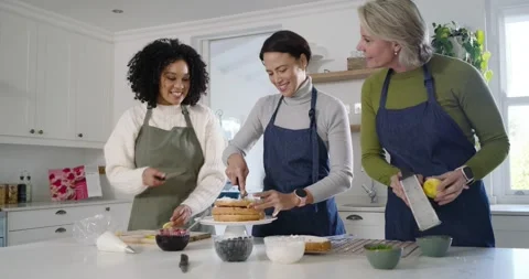 Diverse female friends assembling and decorating layered cake on stand, center Stock Footage 344681546
