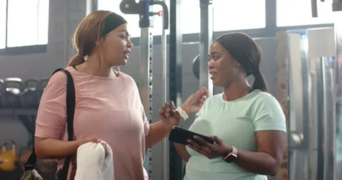 Diverse female friends pointing at tablet screen, consulting workout plan near Stock Footage 340986992