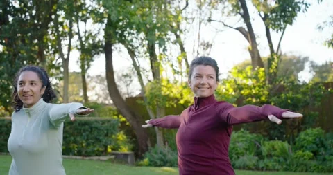 Diverse female friends practicing open-armed pose in zip-up tops in yard Stock Footage 342031684