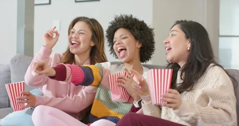 Diverse female friends teasing kernel, munching popcorn from striped buckets Stock Footage 335808615
