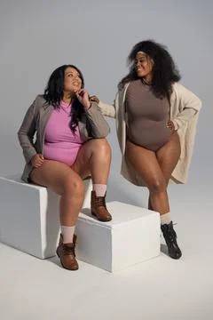 Diverse female models posing in studio with backdrop, wearing bodysuits and Stock Photos