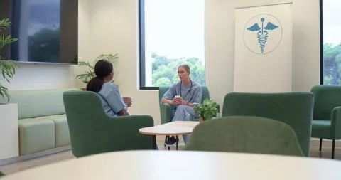 Diverse female nurses sitting in lounge holding cups, wearing stethoscope, Stock Footage 343240134