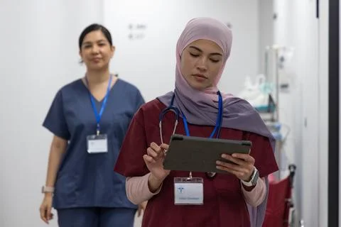 Diverse female nurses using tablet while wearing hijab, stethoscope and ID Stock Photos
