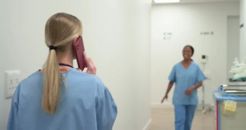 Diverse female nurses walking ward hall, blonde nurse talking on phone toward Stock Footage 341393586