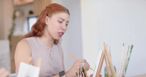 Diverse female pair, camera revealing red-haired painter in studio grabbing Stock Footage 337286412