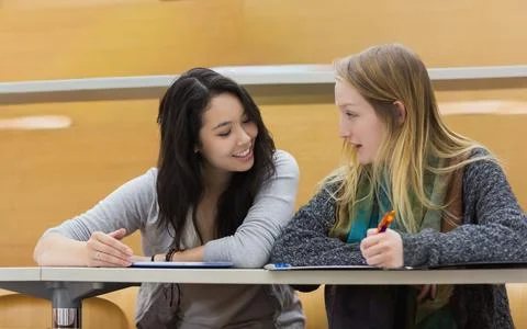 Diverse female students sitting side-by-side in lecture hall, writing notes with Stock Photos