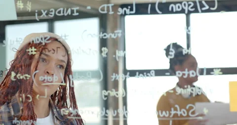 Diverse female team brainstorming code on glass board in modern office, focused Stock Footage 311495574