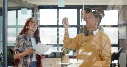 Diverse female team collaborating on coding project, writing on glass board in Stock Footage 311495504
