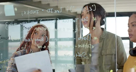 Diverse female team collaborating on coding project, writing on glass board in Stock Footage 311495508