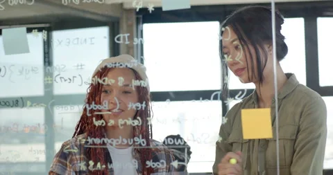 Diverse female team collaborating on coding project, writing on glass board in Stock Footage 311495528