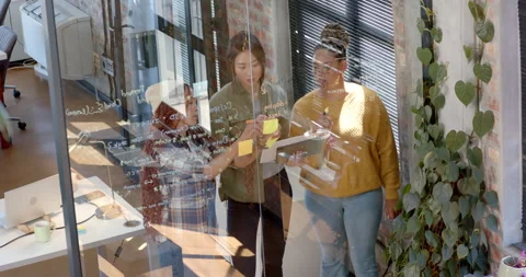 Diverse female team collaborating on coding project, writing on glass wall in Stock Footage 311495569