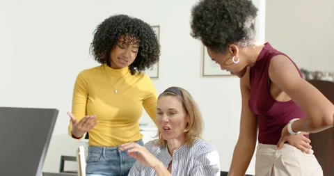 Diverse female team leaning in pointing editing laptop as seated peer showing Video stock 337026422