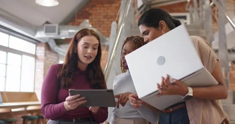 Diverse female team in loft left woman tapping tablet right woman angling laptop Stock Footage 339680255