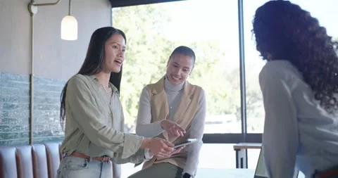 Diverse female team opening tablet at office table, pointing at sheets, using Stock Footage 344670542