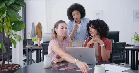 Diverse female team at table in office standing coworker leaning in pointing at Stock Footage 341469176
