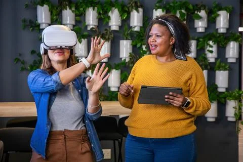 Diverse female team testing VR headset at office while guide holding tablet Stock Photos