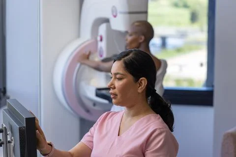 Diverse female tech in scrubs using console in clinic while female patient Stock Photos